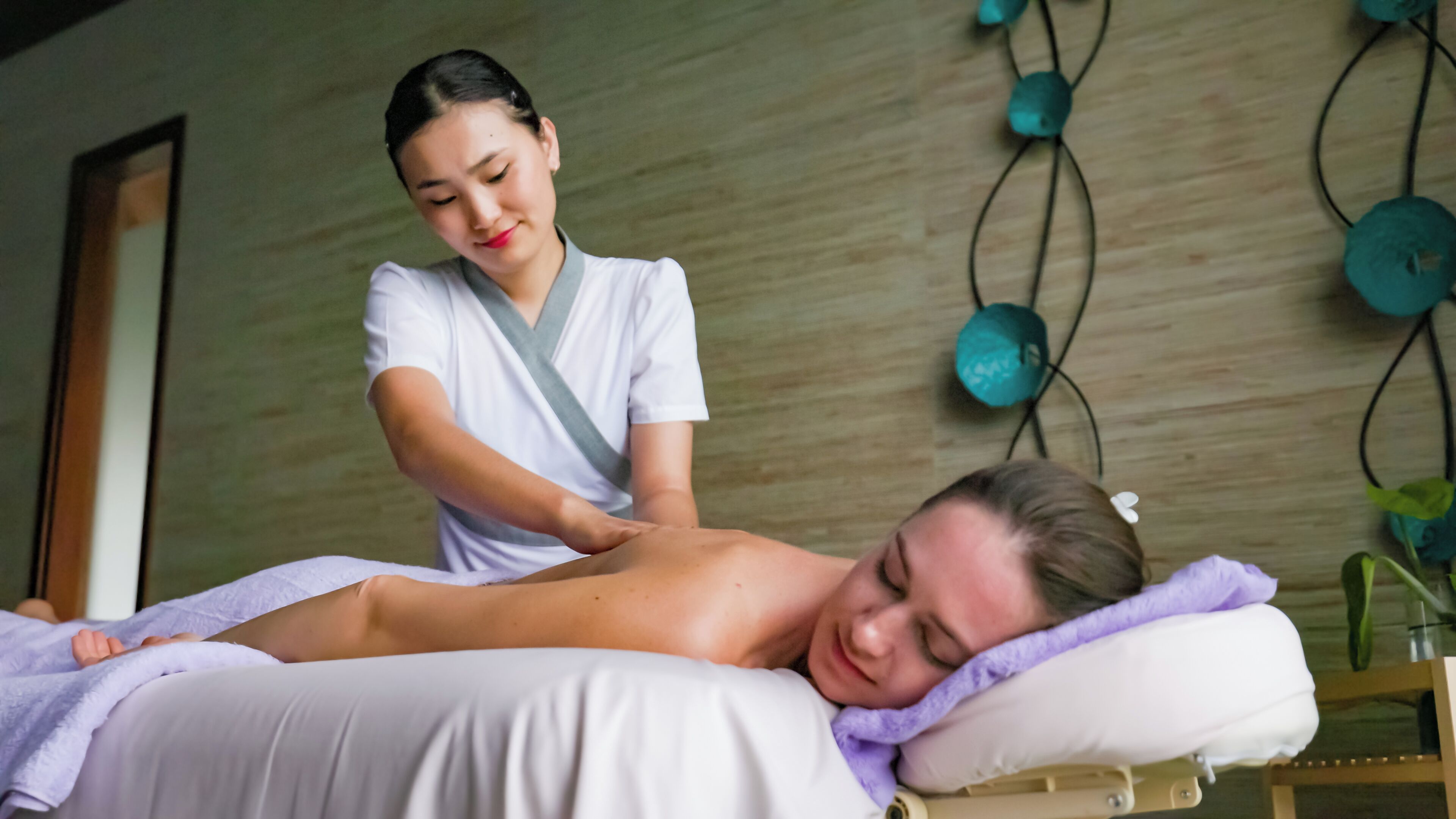 Une séance de massage dans une pièce dont un mur est en bois et qui contient une table de massage.