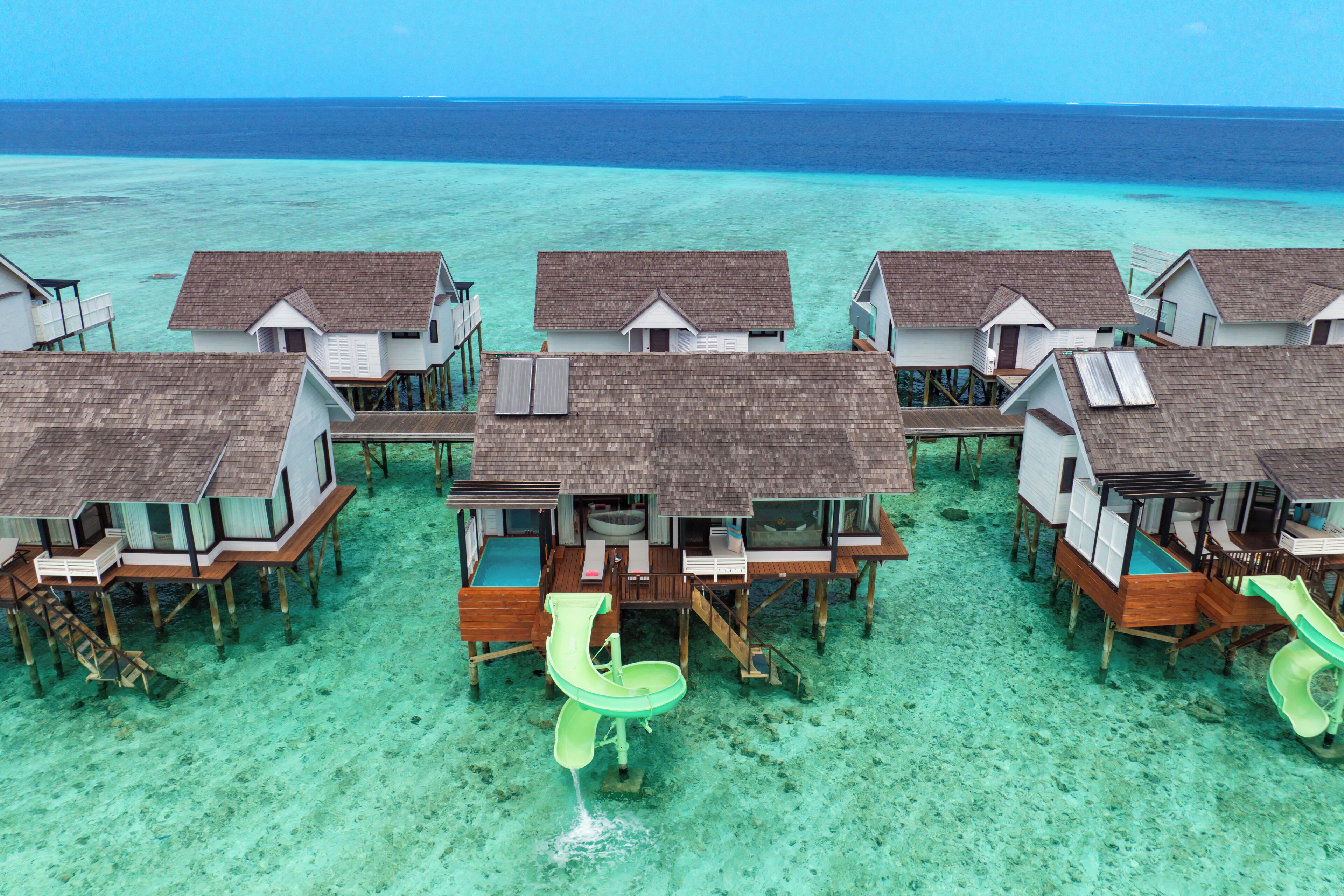 Overwater bungalows with wooden decks and a water slide.