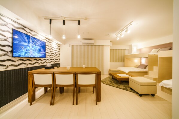 Un salon moderne comprenant un coin repas, un téléviseur fixé au mur et un lit avec une tête de lit.