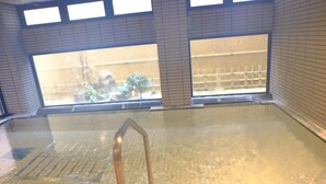 An indoor swimming pool with clear glass walls, a metal ladder, and tiled flooring. - West Inn Fuji-Yoshida (Fujiyoshida)