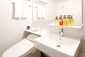 A modern bathroom with a white sink, mirror, and toilet. There are toiletries on the countertop and a towel rack above the mirror. - Hotel New Omi (Omihachiman)