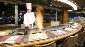 A restaurant with a large dining table, chairs, and a view of the city at night. - Hotel New Omi (Omihachiman)
