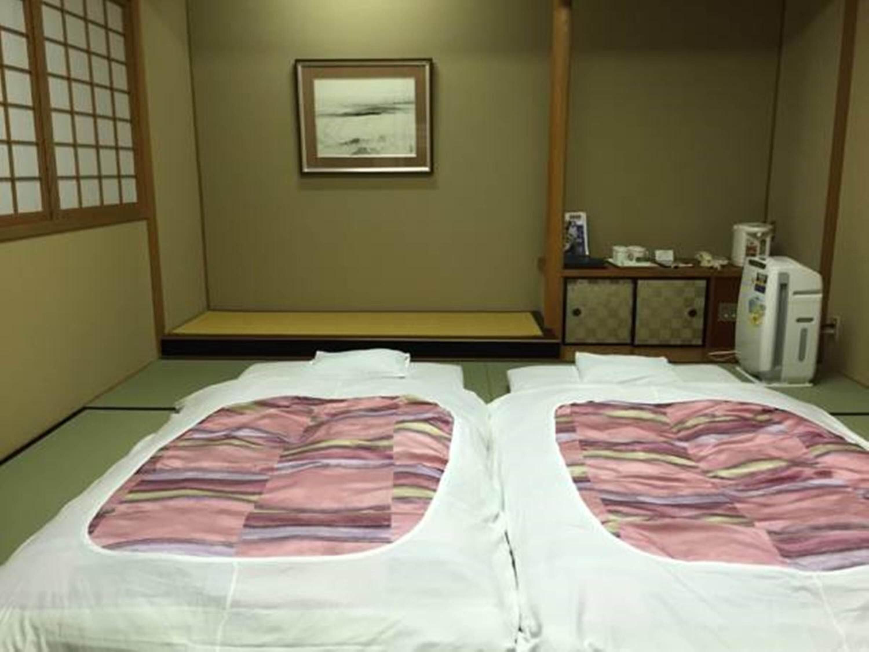 Una habitación de estilo japonés tradicional con suelo de tatami, un banco de madera bajo, un mueble pequeño y un refrigerador.
