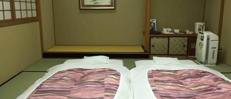 Una habitación de estilo japonés tradicional con suelo de tatami, un banco de madera bajo, un mueble pequeño y un refrigerador.
