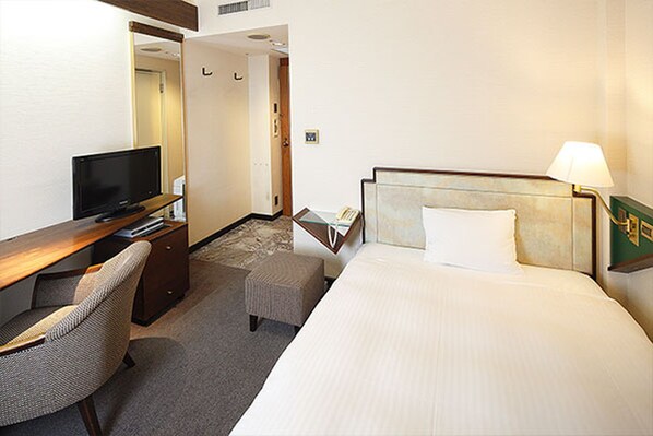 A hotel room with a bed, a desk with a television, a chair, and a lamp. - Hotel New Omi (Omihachiman)