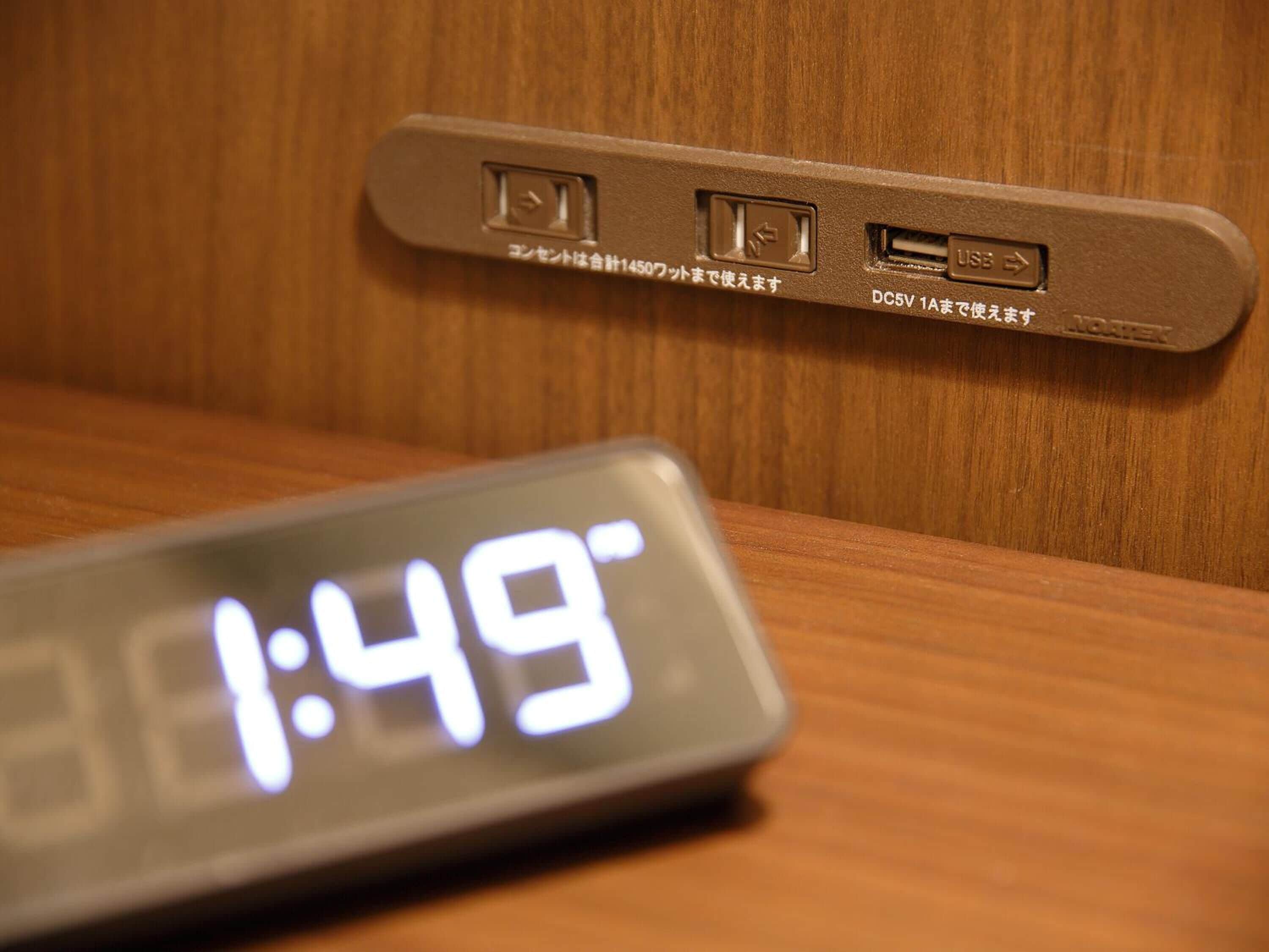 Une horloge numérique affichant 1 h 49 et un port de chargement USB sur une surface en bois.