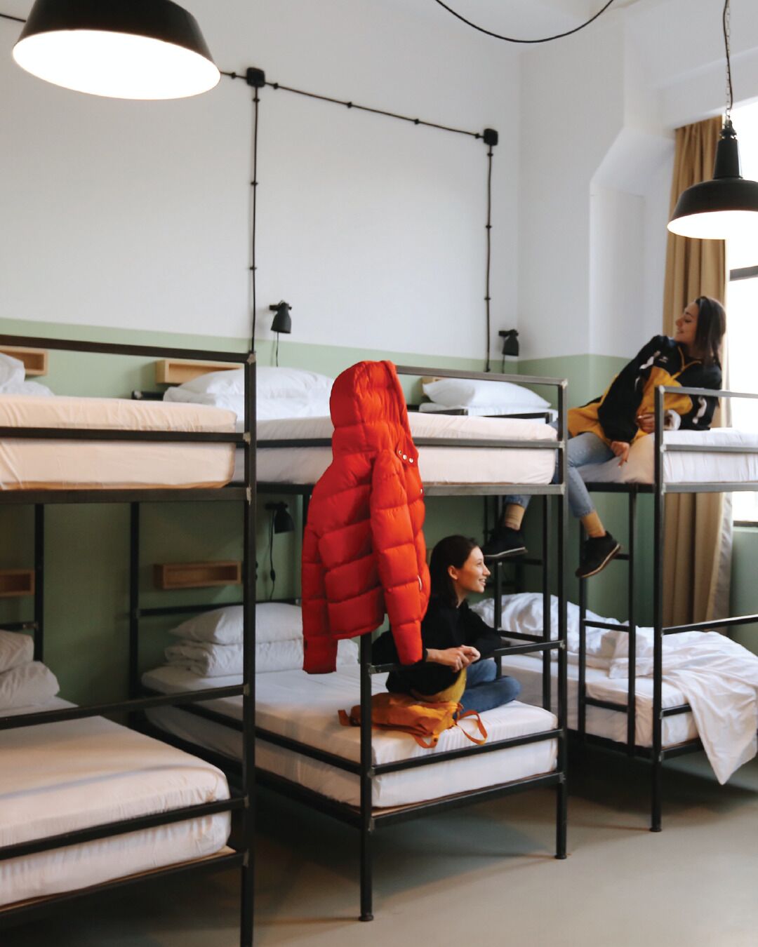 Des lits superposés avec une veste rouge suspendue, une lampe et une fenêtre avec des rideaux.