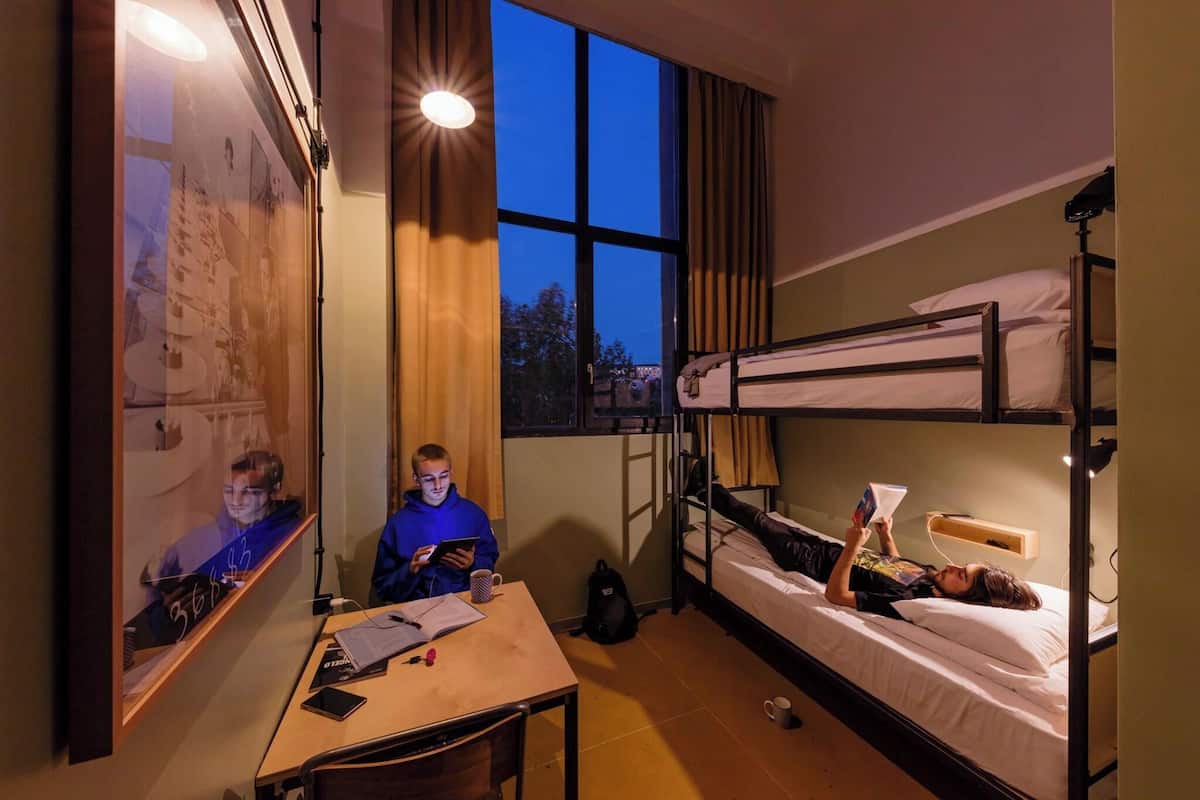 Ein Schlafsaalzimmer mit Etagenbetten, einem Schreibtisch und einem Fenster mit Vorhängen.