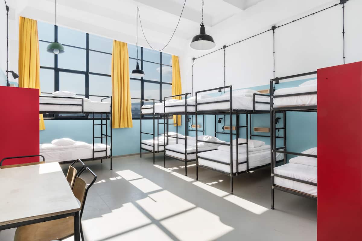 Ein Schlafsaalzimmer mit Etagenbetten, einem Tisch, Stühlen und großen Fenstern mit Vorhängen.
