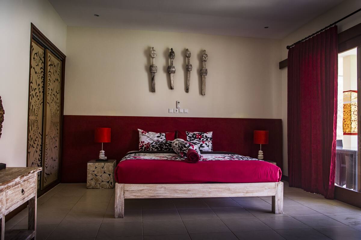 A bedroom with a wooden bed, red curtains, and decorative wall art.