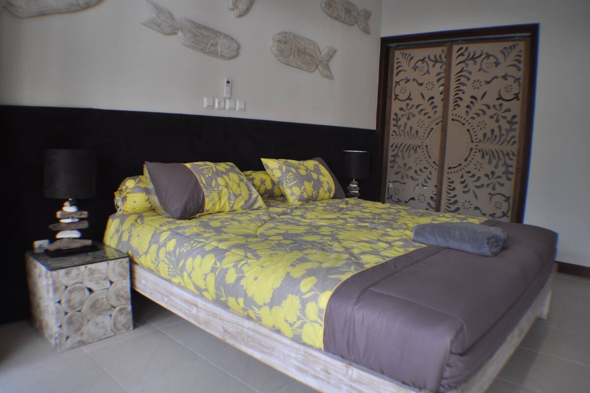A bedroom with a bed, pillows, a nightstand, a lamp, and a decorative wall piece.