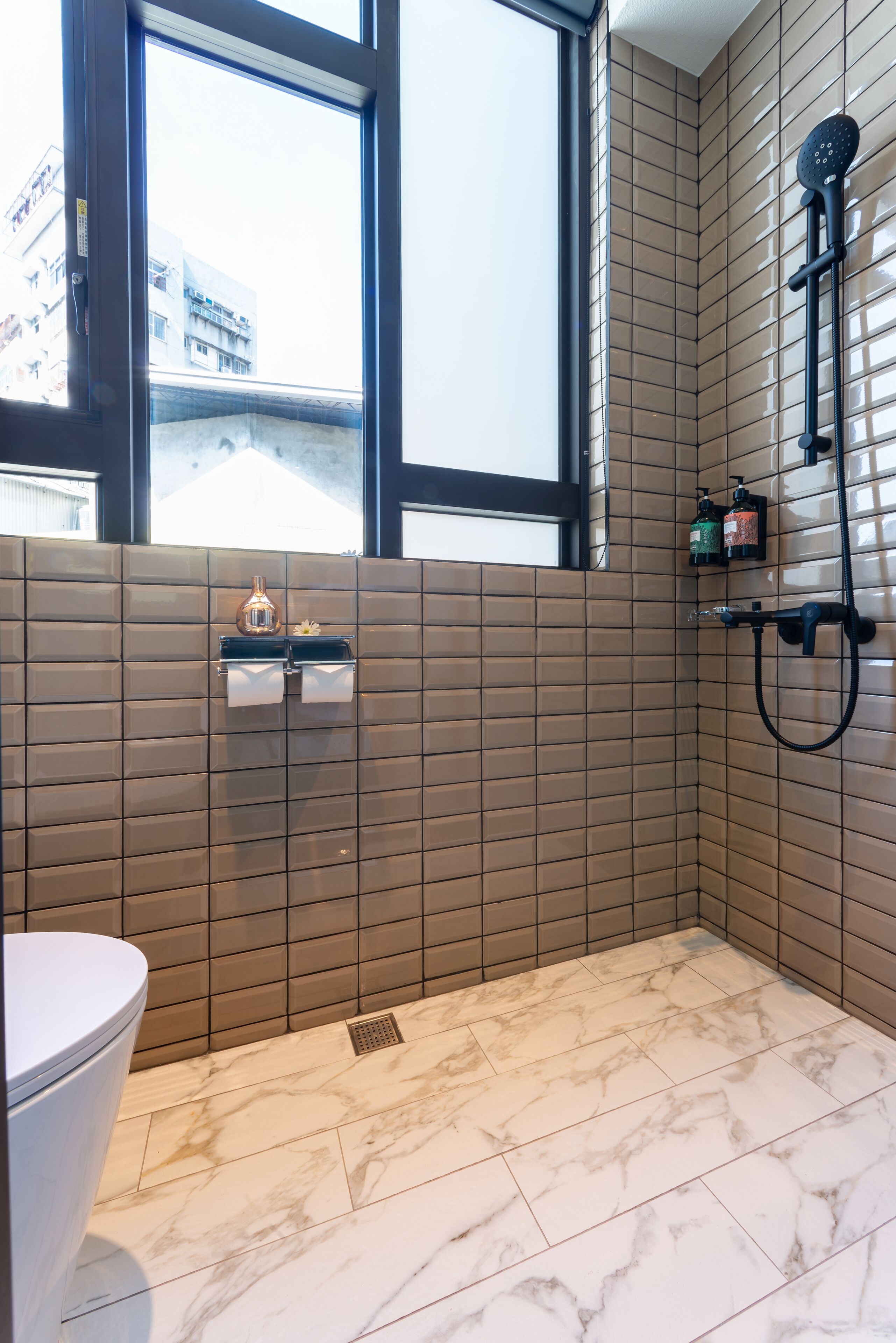 A modern bathroom with a toilet, a shower, and a window.