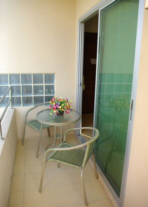 A balcony with a glass table, two wicker chairs, and a flower arrangement. - Mild Guesthouse (Patong)
