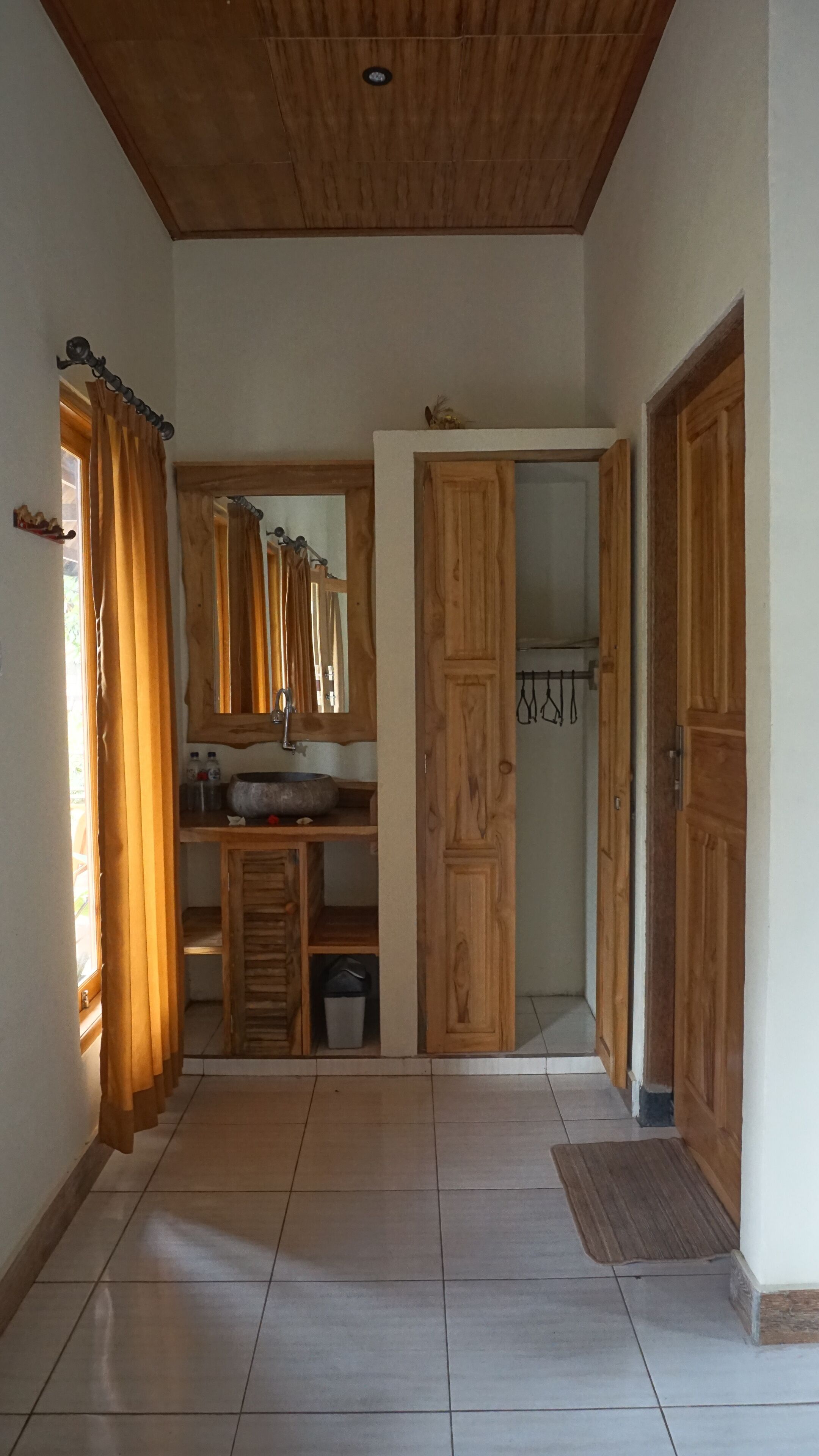 A hallway with wooden doors, a mirror, a sink, and a window with curtains.