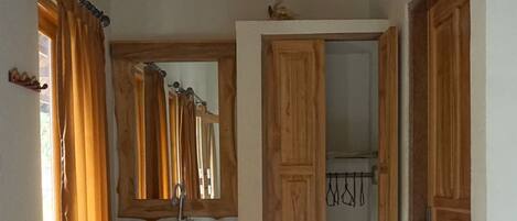 A hallway with wooden doors, a mirror, a sink, and a window with curtains.