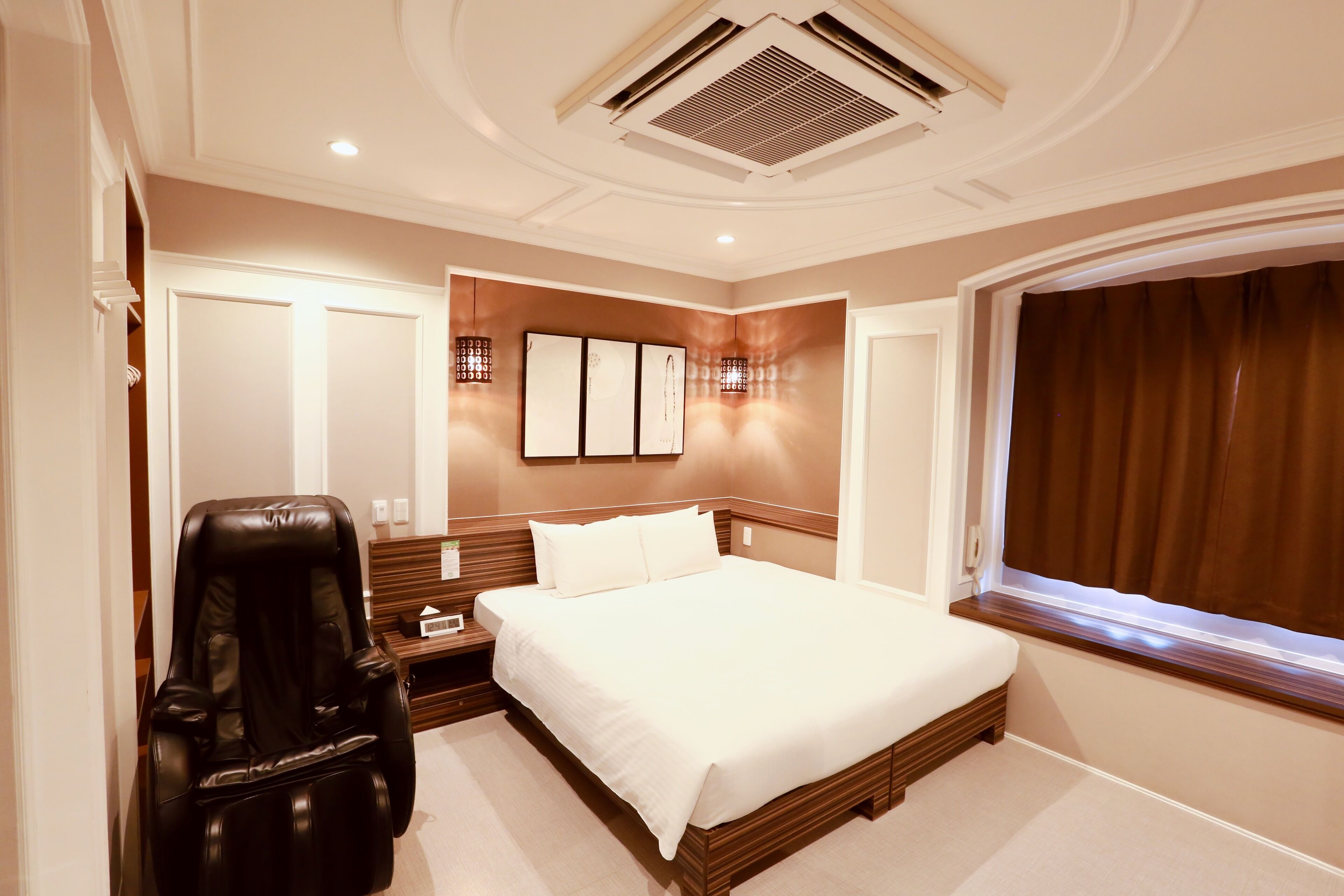 Habitación de hotel con una cama grande, una silla de masajes, una mesita de noche y una ventana con cortinas.