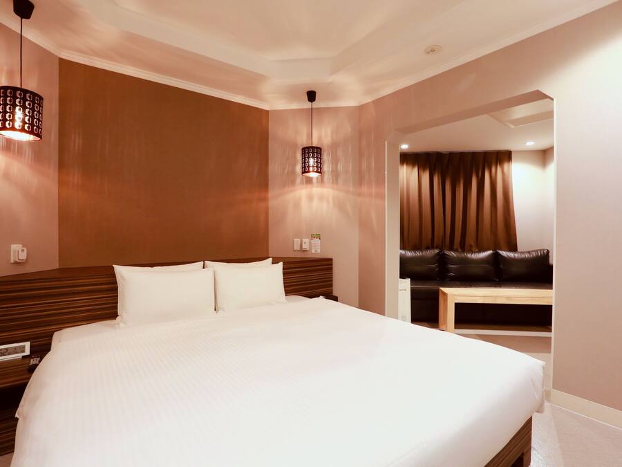 A hotel room with a large bed, two bedside tables, a wooden headboard, a nightstand, a digital clock, and a mirror.