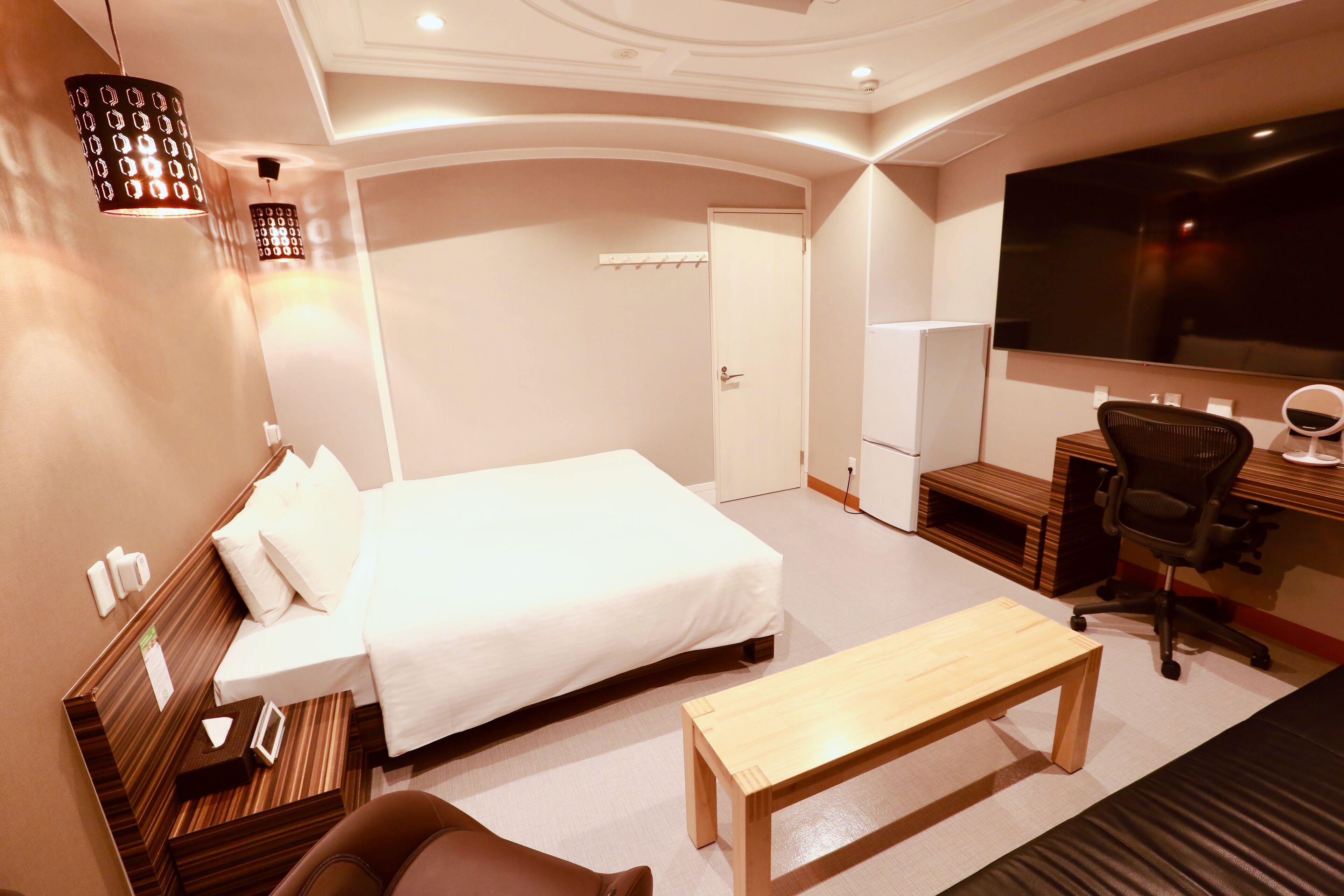 A hotel room with a bed, a desk, a chair, a TV, and a lamp.