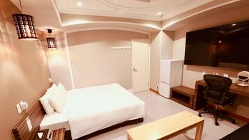 A hotel room with a bed, a desk, a chair, a TV, and a lamp.