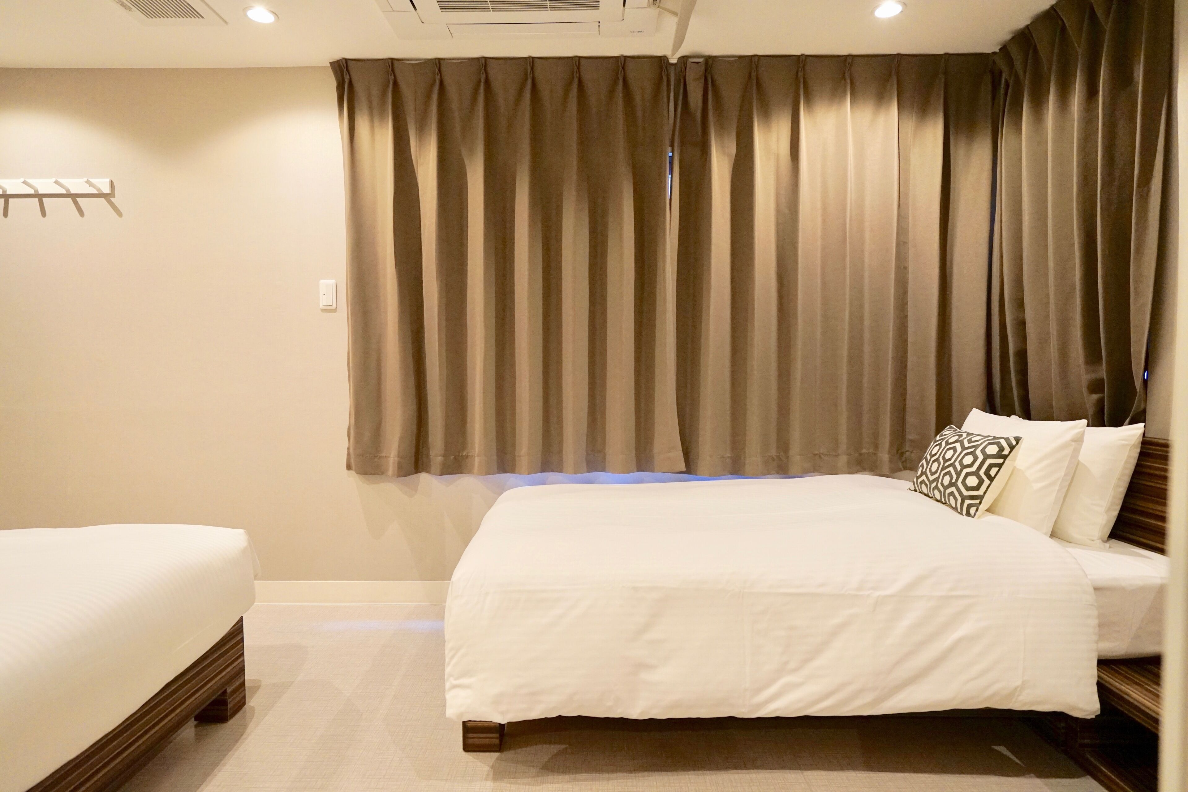A hotel room with a large bed, a smaller bed, and a headboard with a patterned pillow.