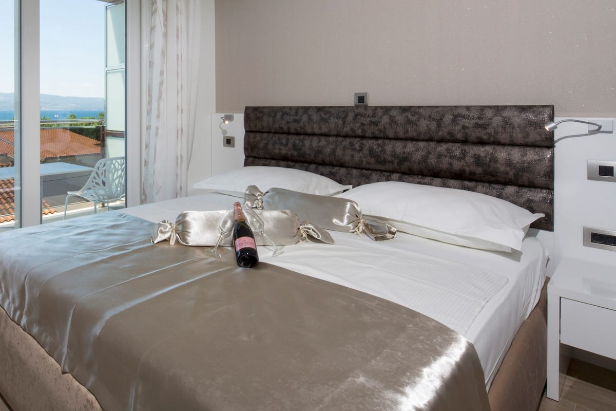 A hotel room with a large bed, a view of the sea, and a balcony with a chair.