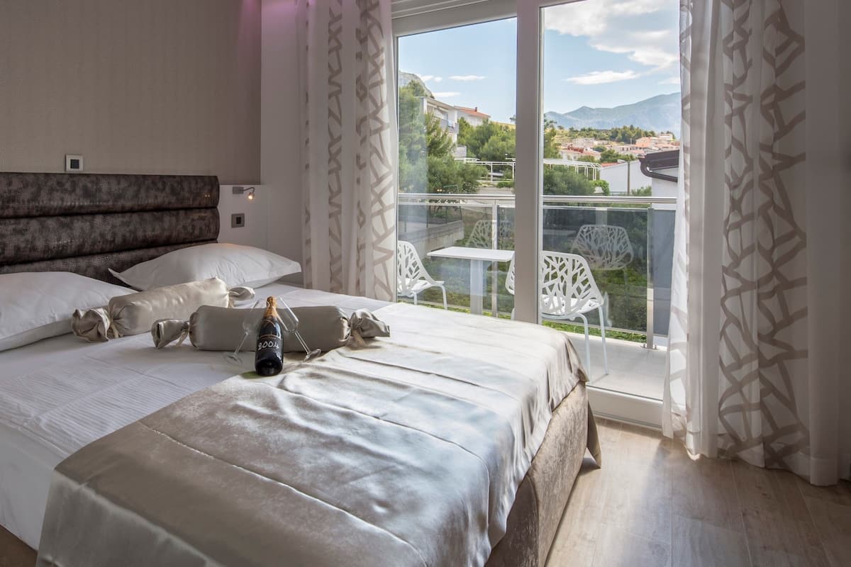 A bedroom with a large bed, a bottle of champagne, and a balcony with white chairs.