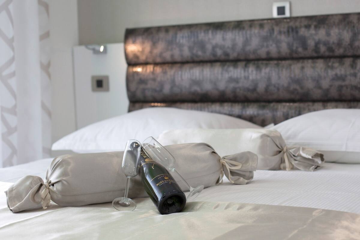 A neatly made bed with a bottle of champagne and a glass on it.