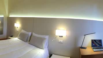Ein Hotelzimmer mit Bett, Nachttisch mit Laptop, Wandfernseher und Kleiderschrank.