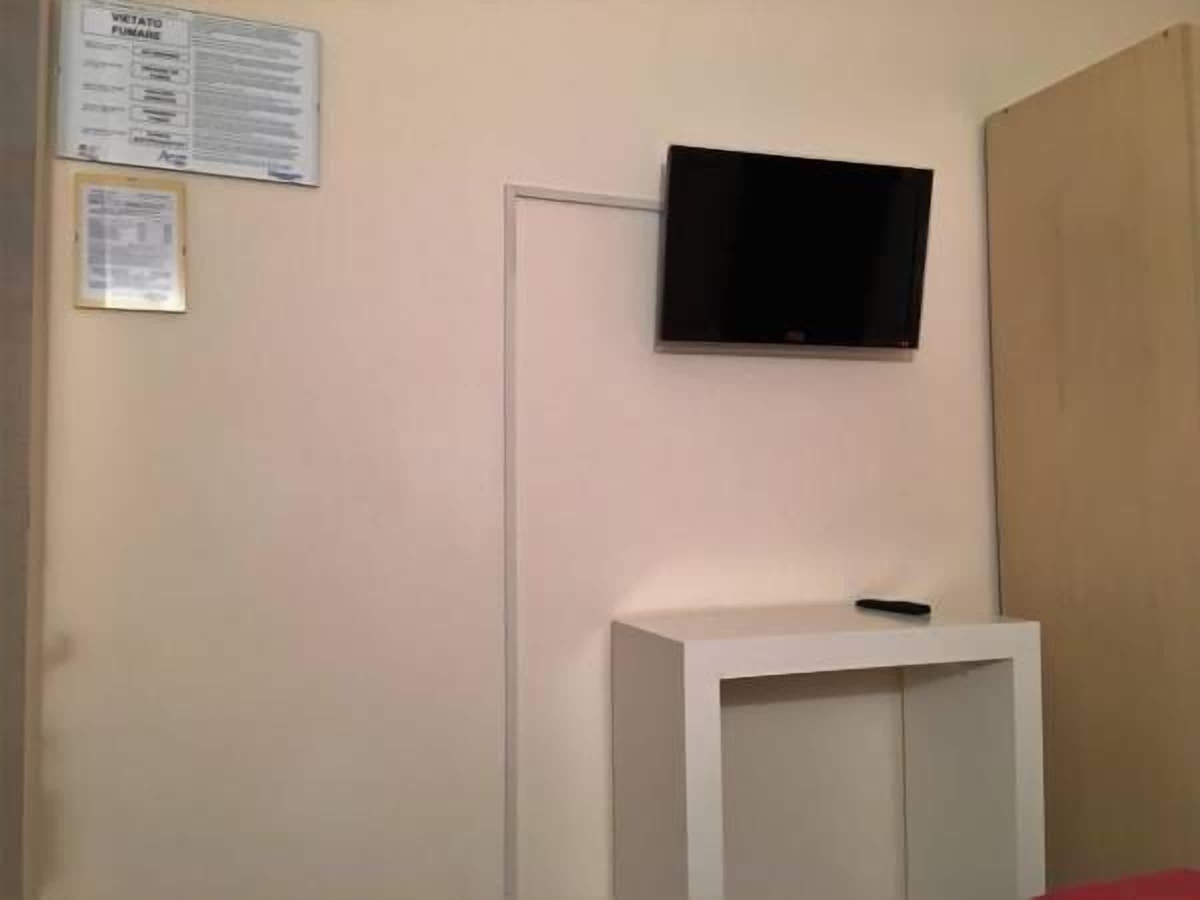 Una habitación con una televisión de pantalla plana montada en la pared, una consola blanca y una pared color beige con dos carteles informativos.