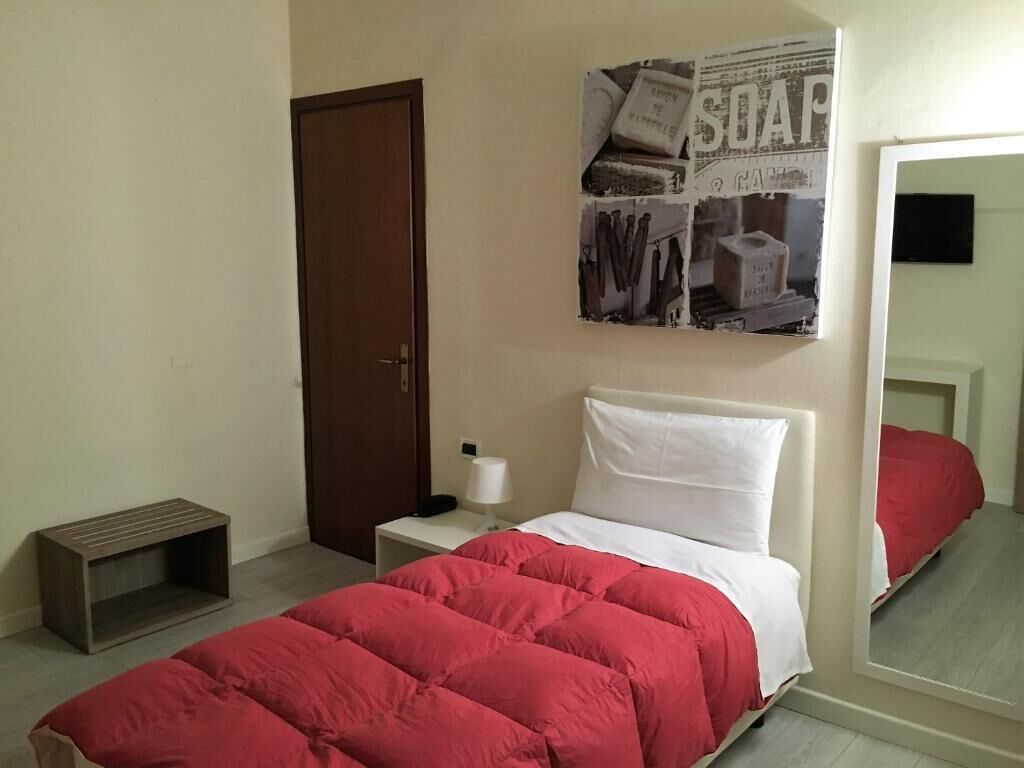 Quarto com cama, mesa de cabeceira, luminária, espelho e porta.