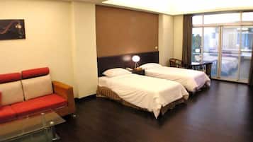 Una habitación de hotel con dos camas, un sofá, un escritorio y un ventanal grande.