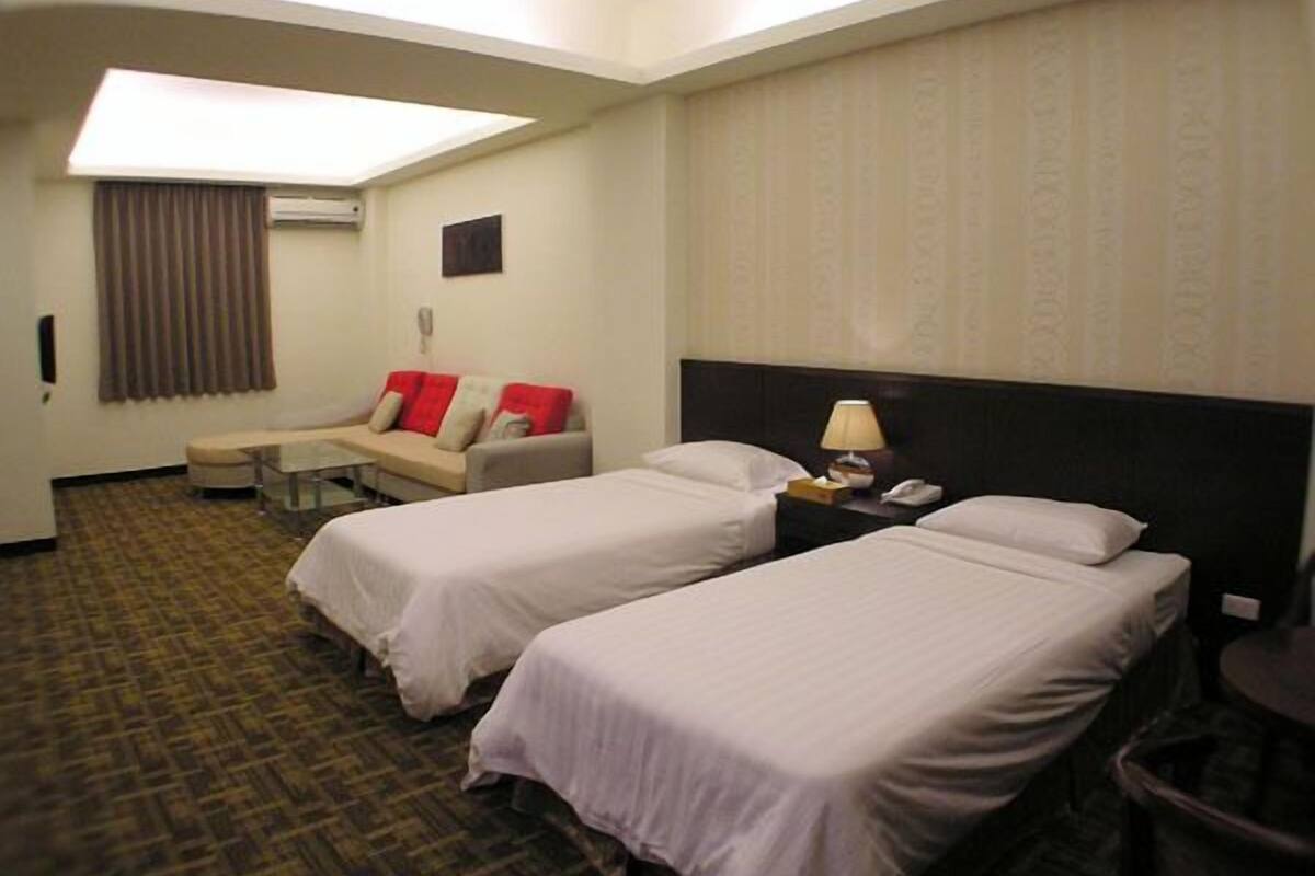 Habitación de hotel con dos camas, un sofá, una mesita y una lámpara.