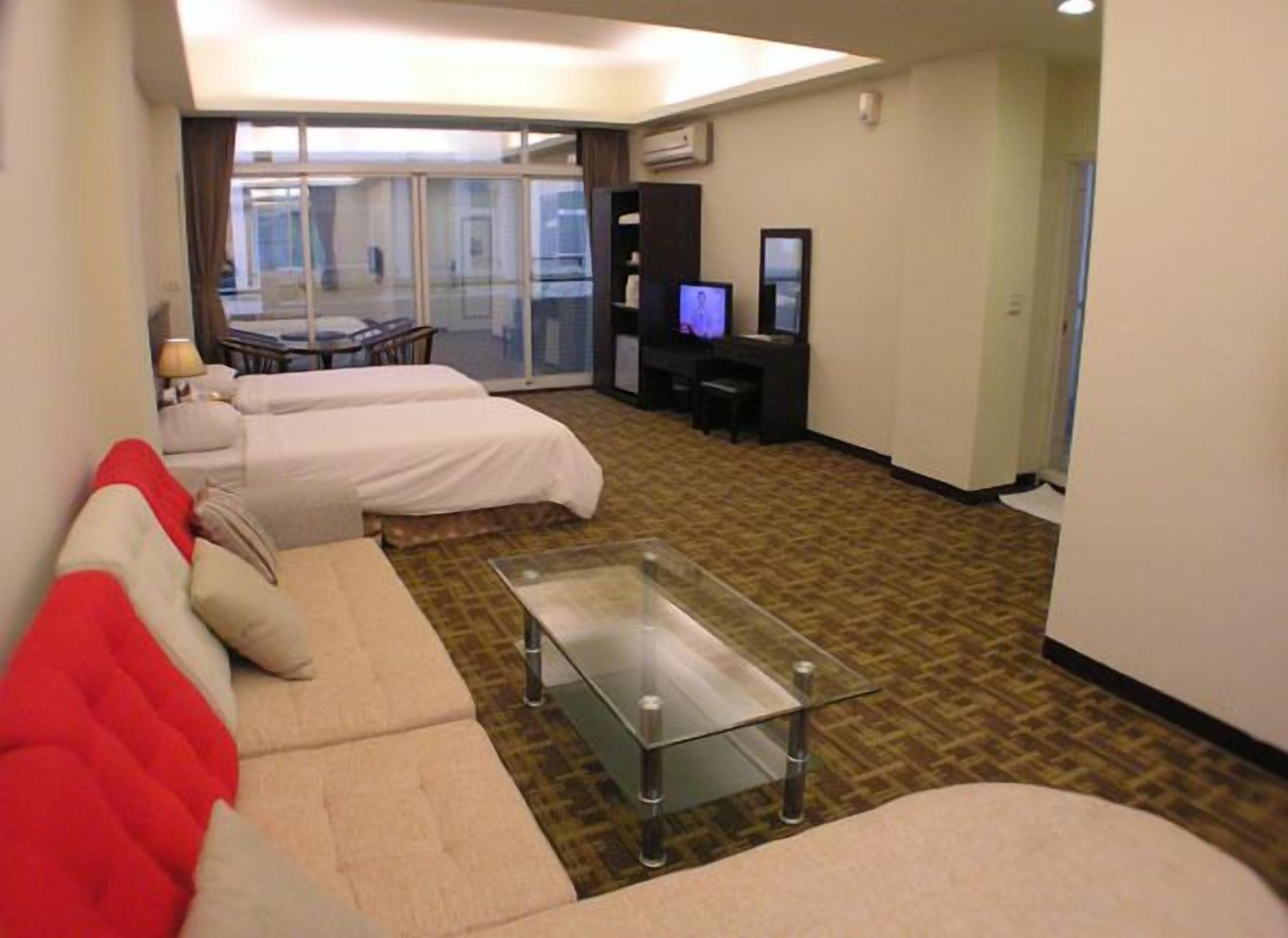 Habitación de hotel con sofá, una mesita de centro de vidrio, televisor y escritorio.