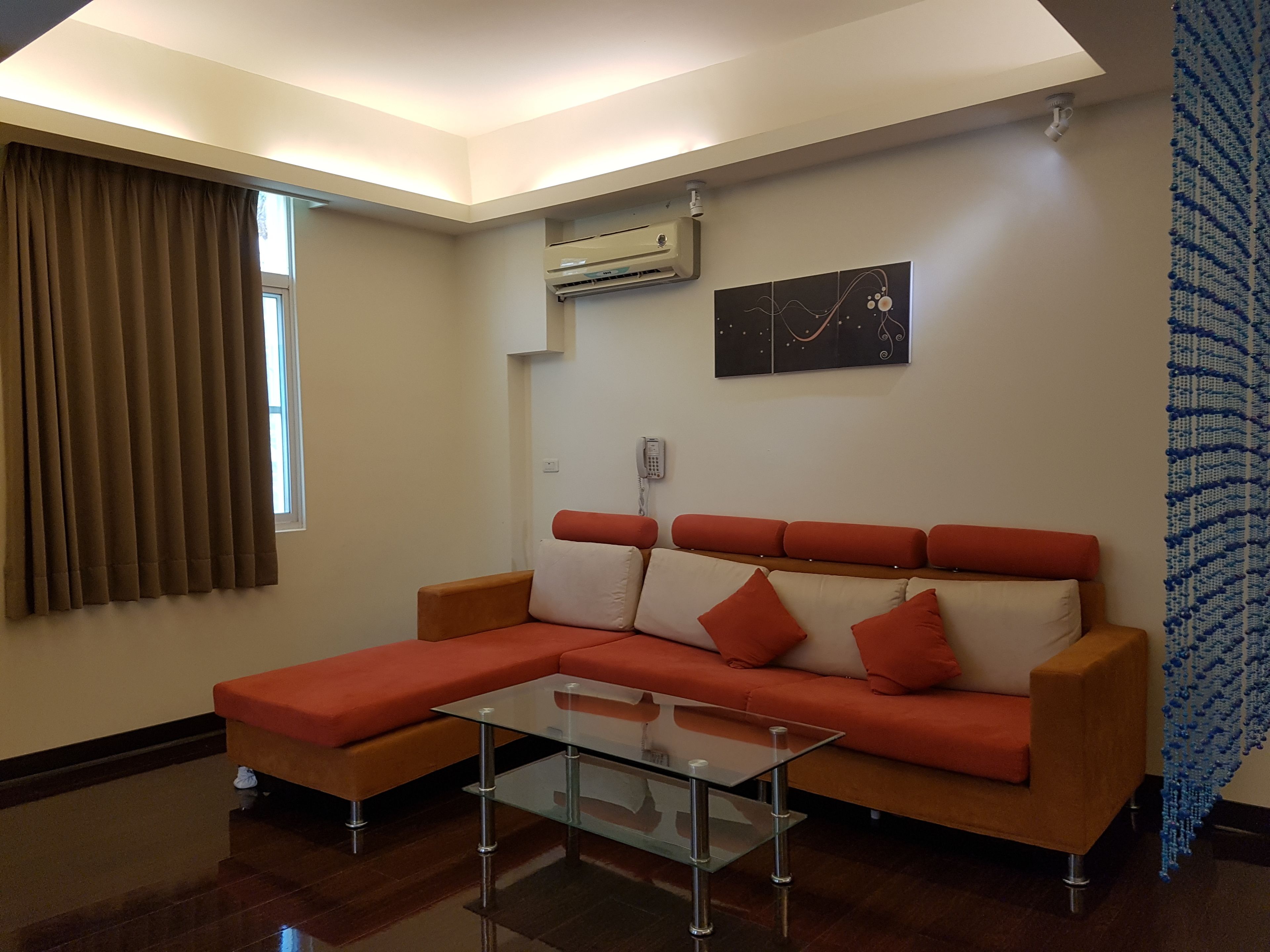 A modern living room with a sectional sofa, a glass coffee table, and an air conditioning unit on the wall.
