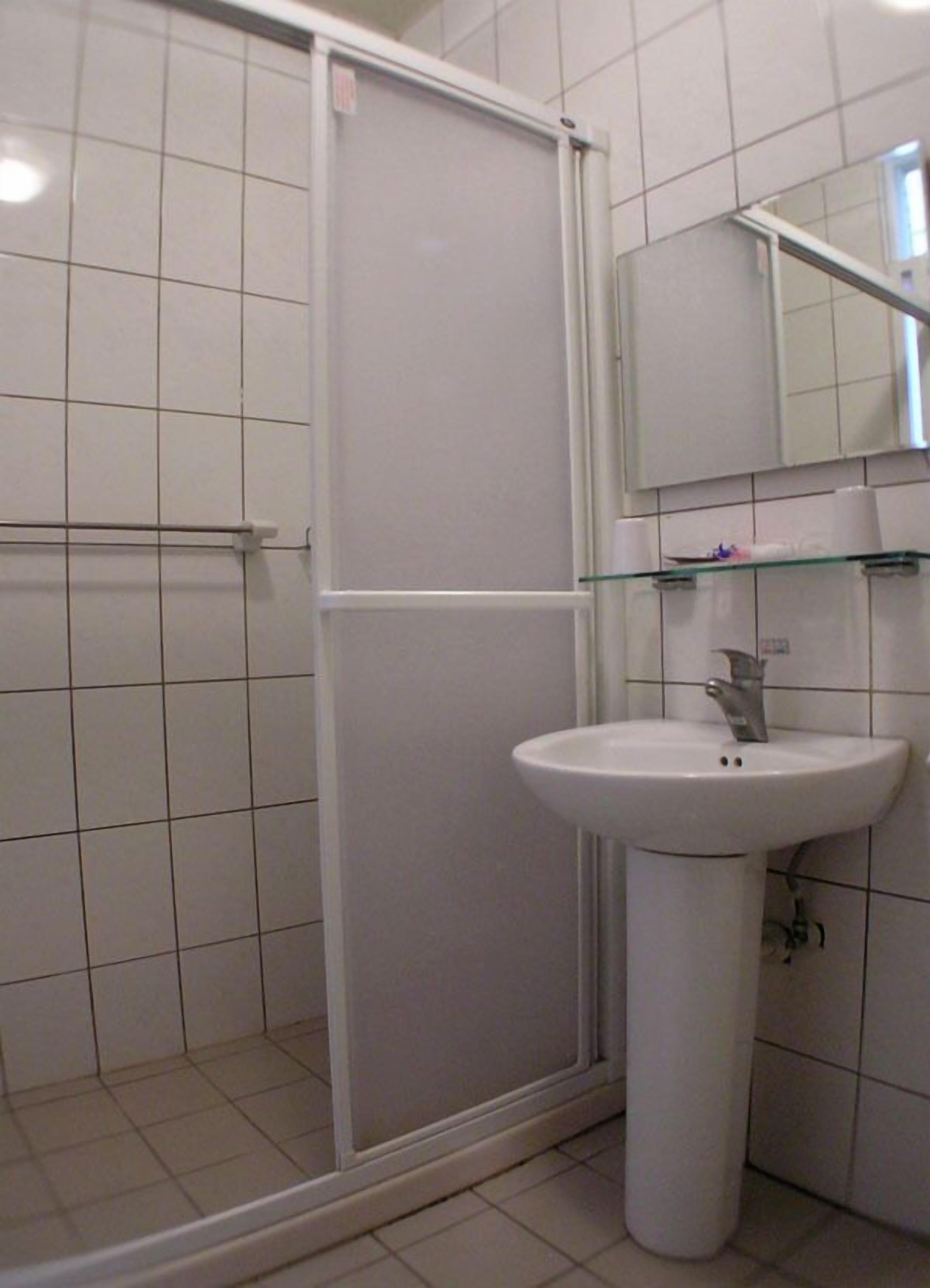 Un baño con un lavabo blanco, cabina de ducha con mampara de vidrio y espejo sobre el lavabo.