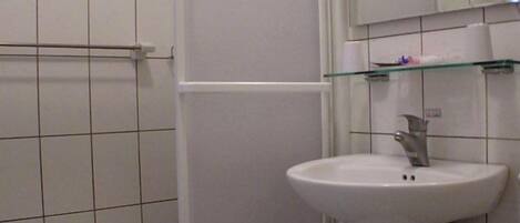 Un baño con un lavabo blanco, cabina de ducha con mampara de vidrio y espejo sobre el lavabo.