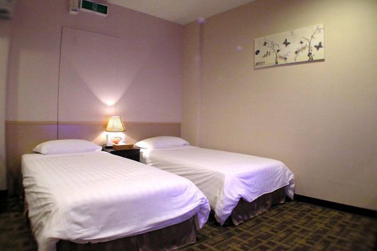 Una habitación de hotel con dos camas individuales, una mesita de noche con lámpara, una obra de arte en la pared y una puerta.