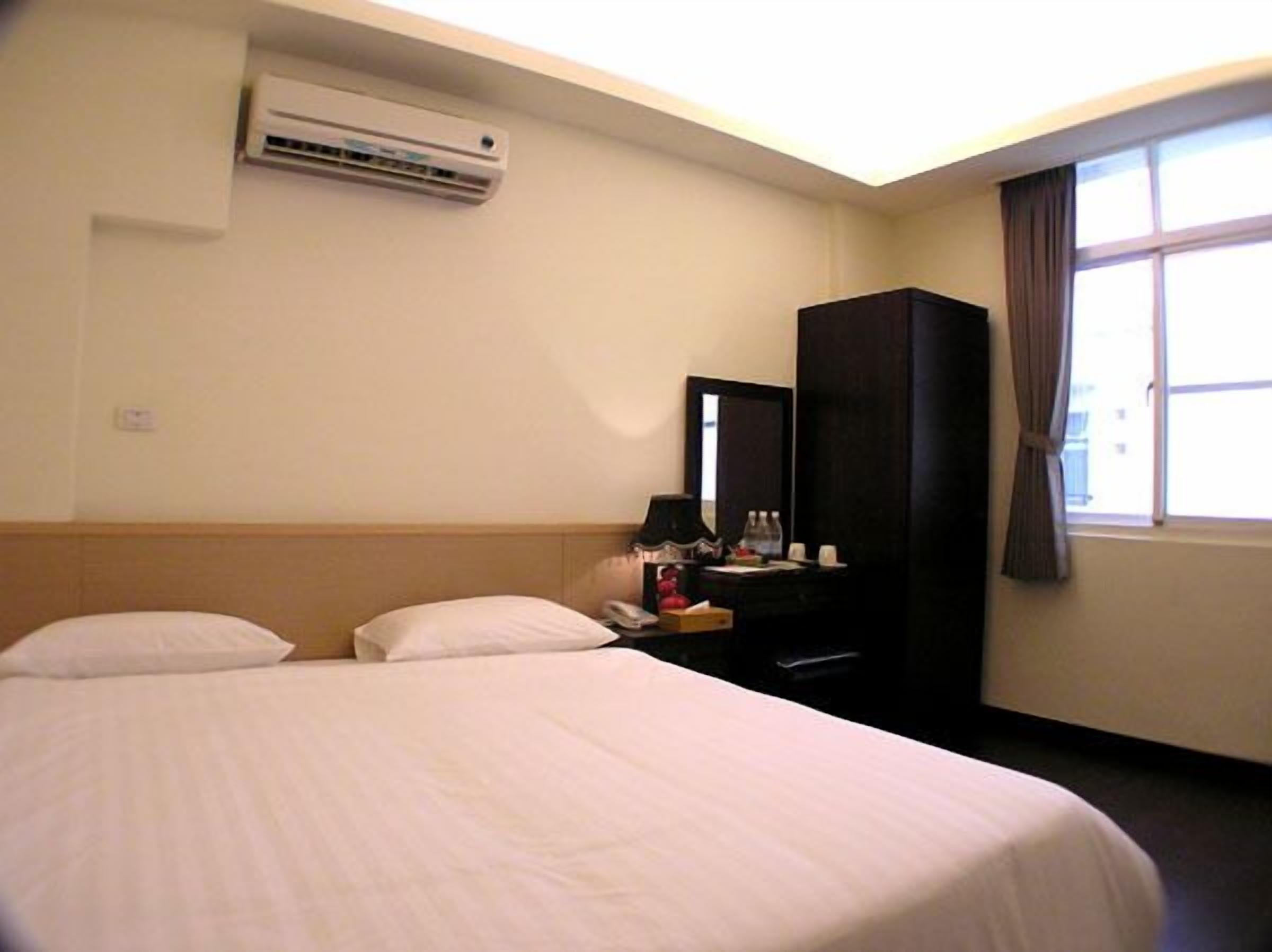 A hotel room with two beds, a desk, a mirror, and an air conditioning unit.