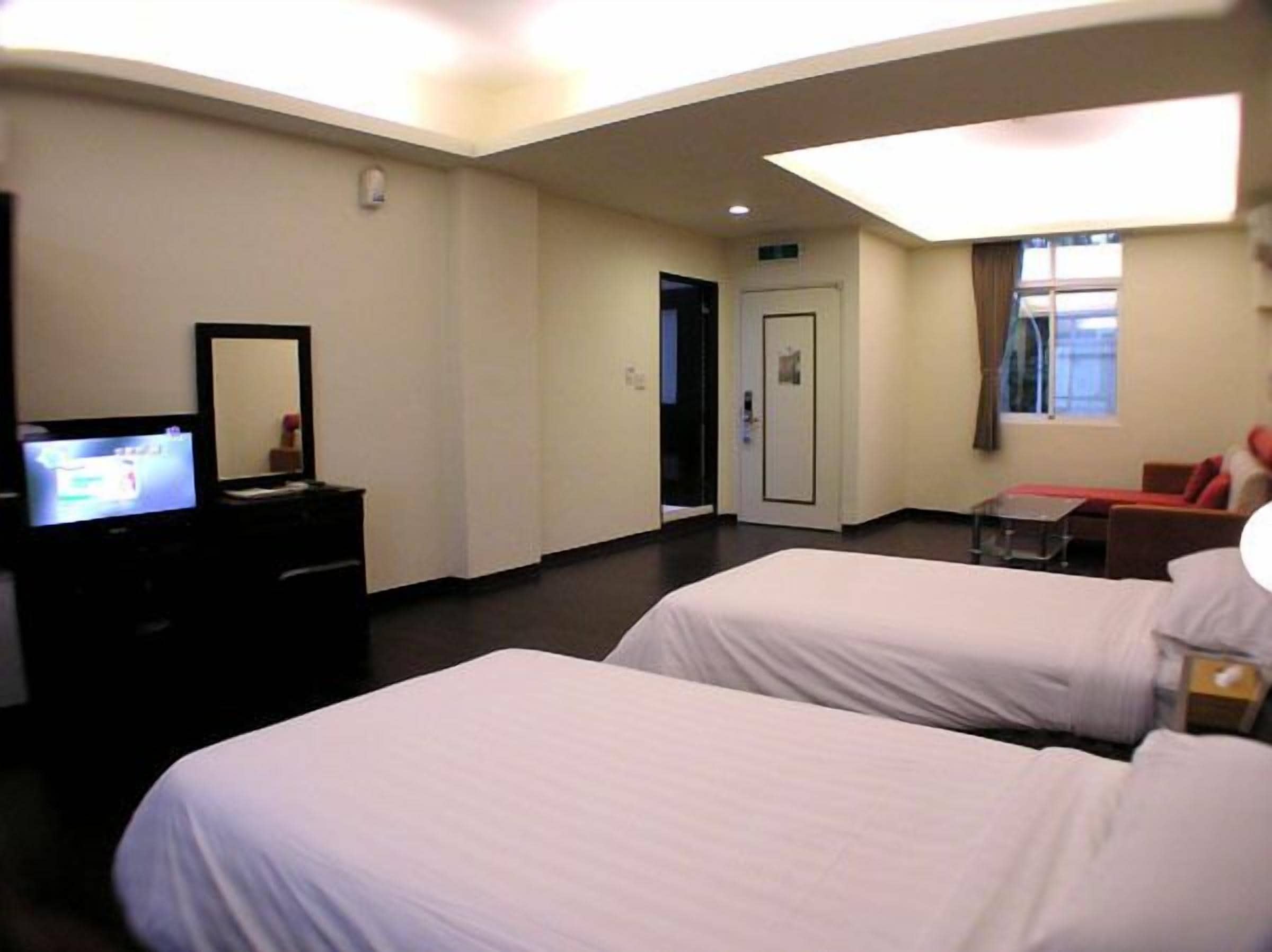 Una habitación de hotel con dos camas, un televisor en una cómoda, una puerta y una ventana.
