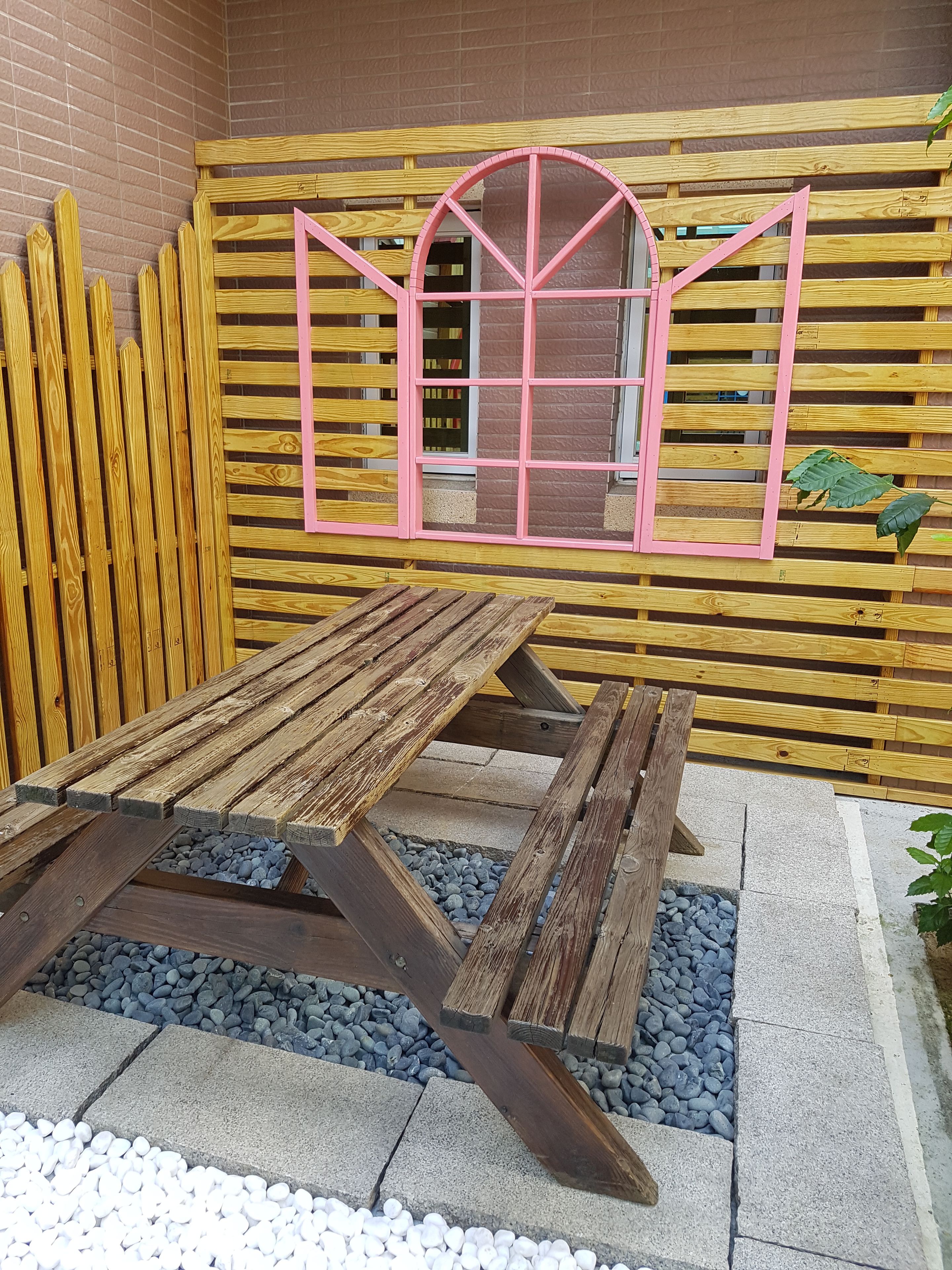 A wooden picnic table with a pink-framed window in the background.