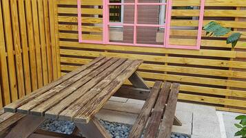 A wooden picnic table with a pink-framed window in the background.