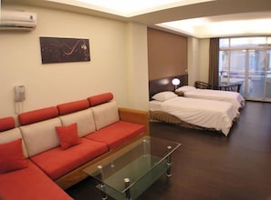 Habitación de hotel con un sofá rojo, dos camas, una mesa de centro de vidrio, un cuadro en la pared y un teléfono.