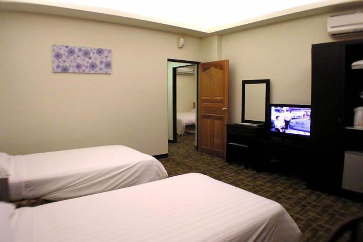 Habitación de hotel con dos camas individuales, televisión, armario y baño visible a través de una puerta abierta.