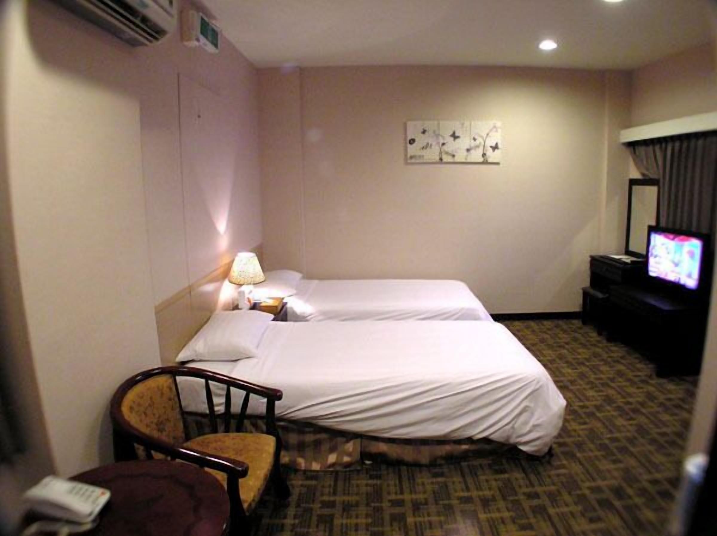 A hotel room with two beds, a chair, a television, and a wall-mounted air conditioner.