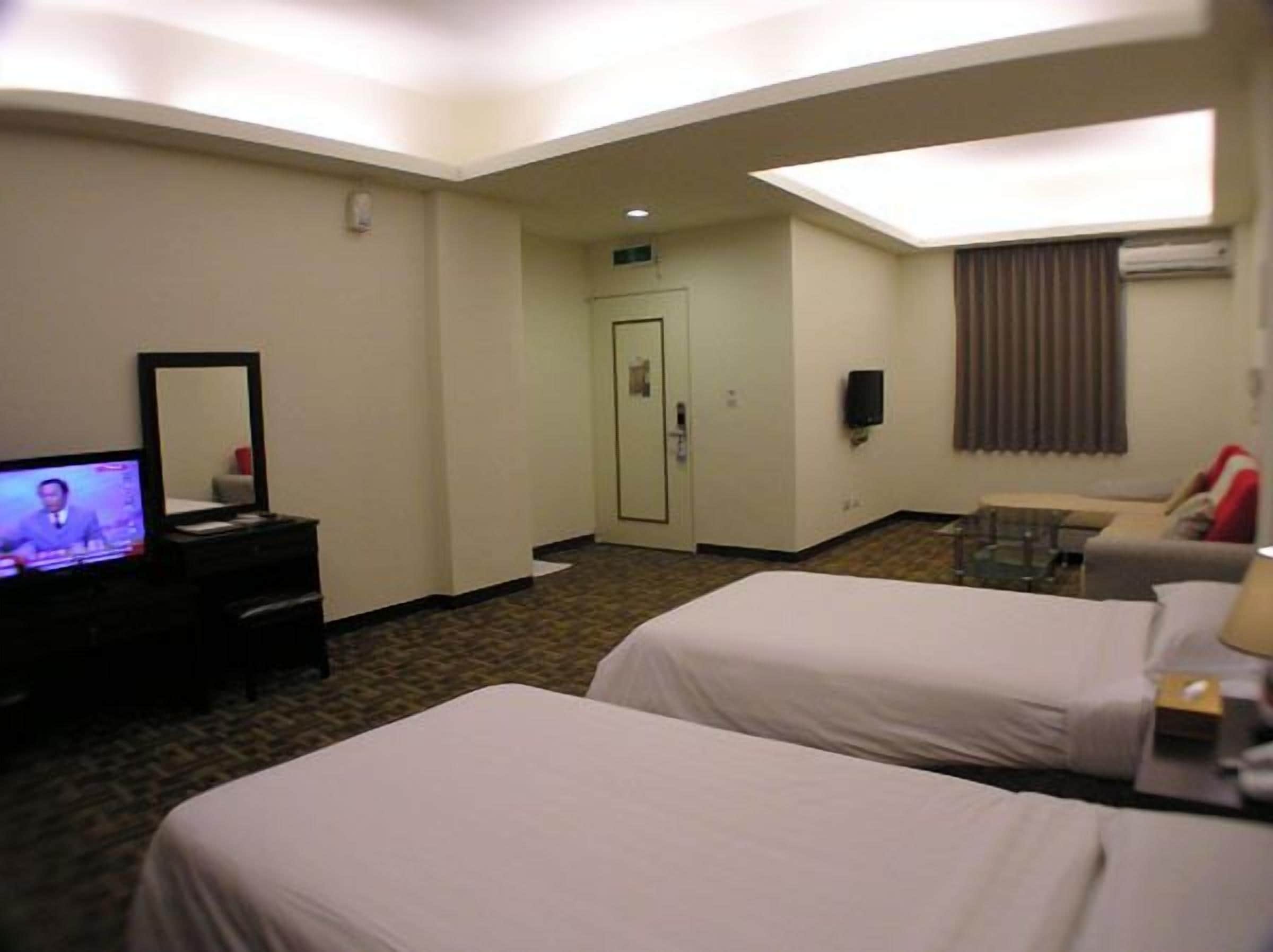 Habitación de hotel con dos camas, televisión, escritorio, silla y ventana con cortinas.