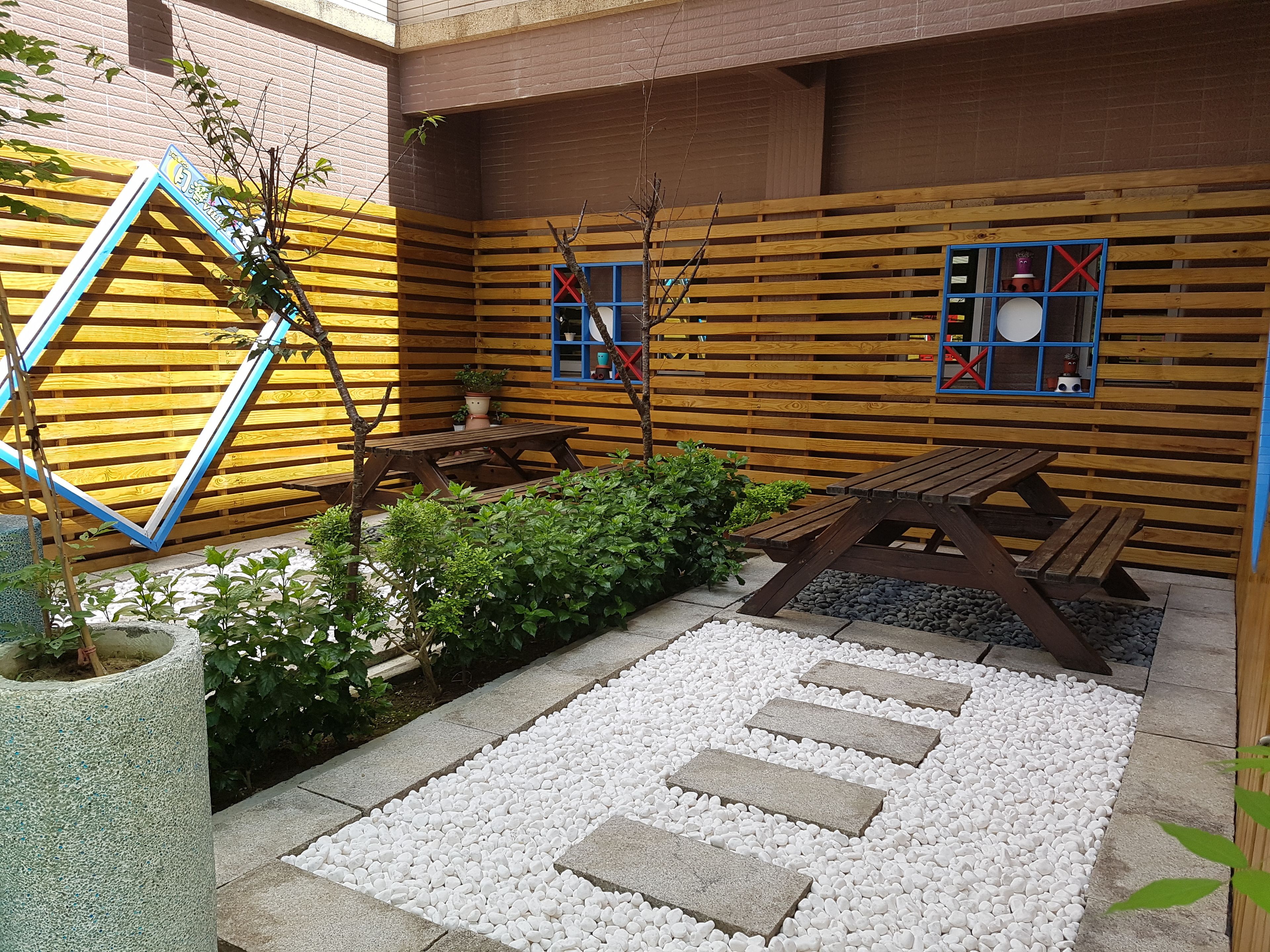 A patio area with wooden benches, a stone pathway, and a brick wall with blue accents.
