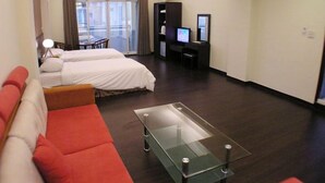 Une chambre d’hôtel avec deux lits, une table basse en verre, un canapé rouge, un bureau avec un ordinateur et une télévision.