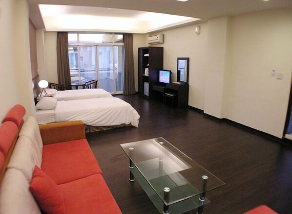 A hotel room with two beds, a glass coffee table, a red sofa, a desk with a computer, and a TV.