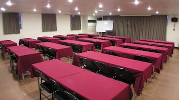 A conference room with rows of tables covered in red tablecloths and black chairs.