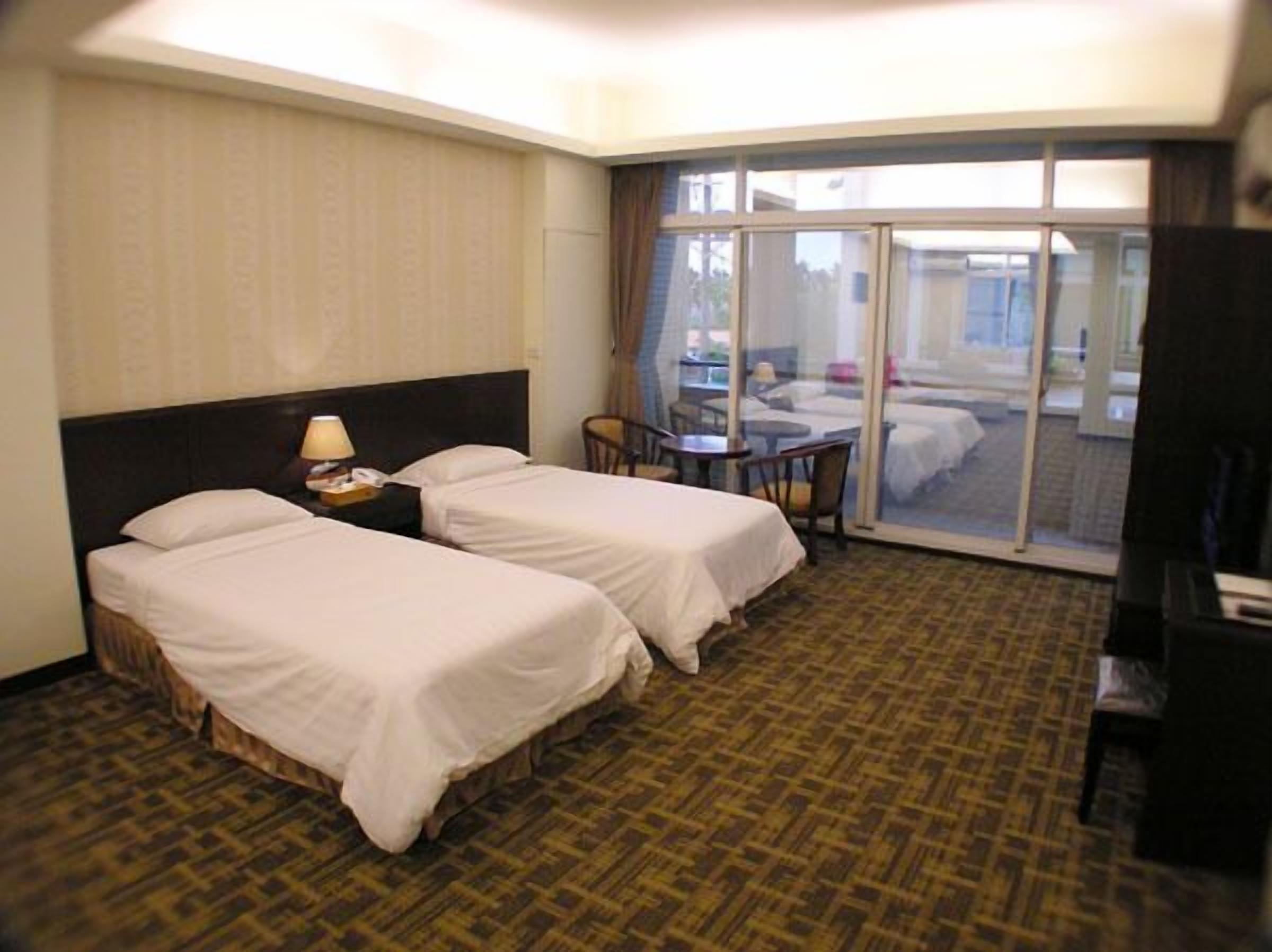 Une chambre d’hôtel avec deux lits, un bureau et une vue sur un espace extérieur aménagé, accessible par une porte vitrée.